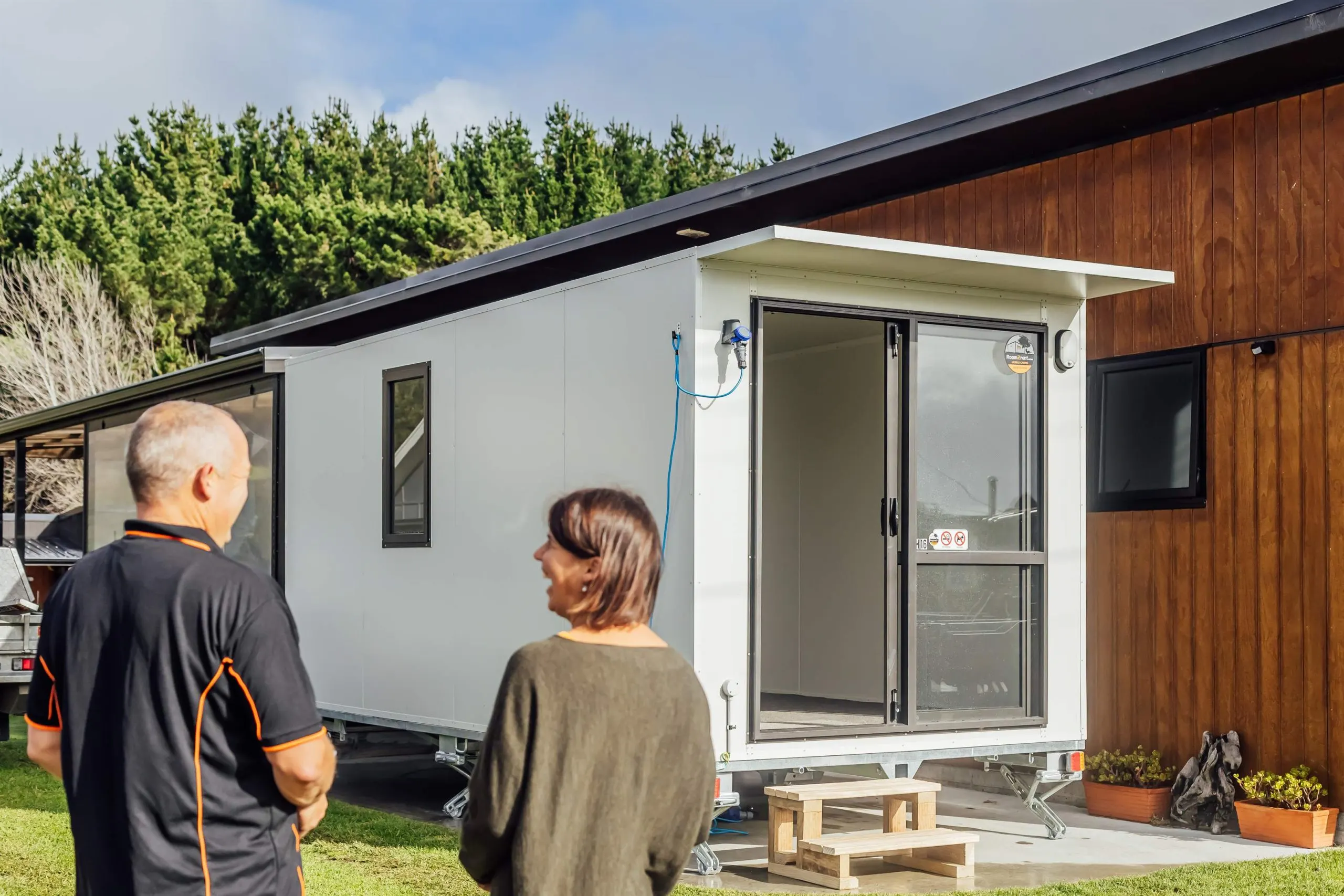 A man and woman stand together in front of a mobile home, smiling and enjoying their time outdoors