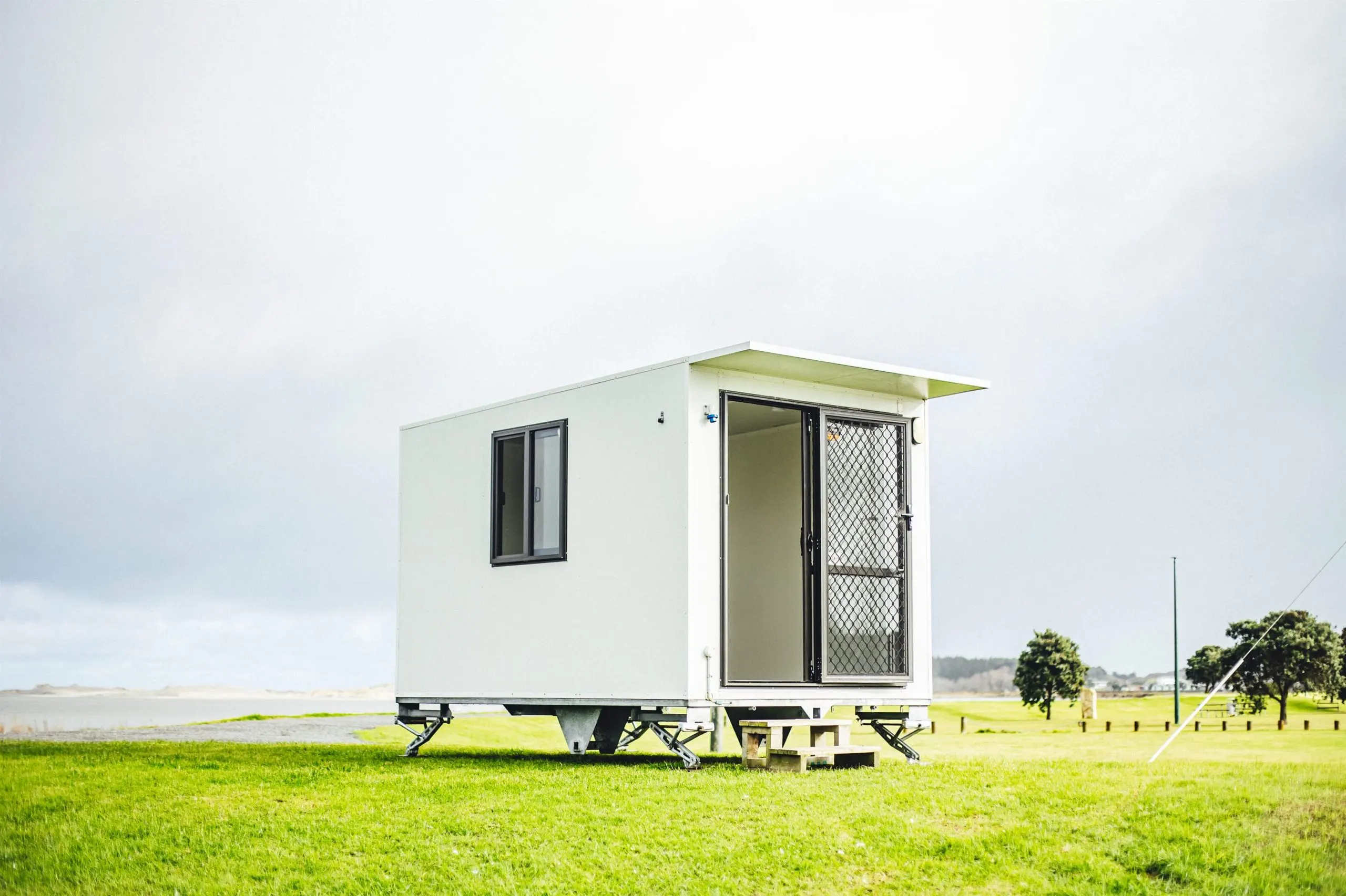 A white mobile home sits on a lush green field, surrounded by grass and open space