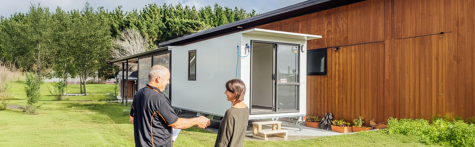 stands in front of a house, looking happy and relaxed in the outdoor setting