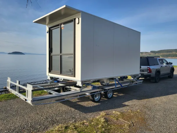 A small white trailer with a car secured on it, positioned on a driveway