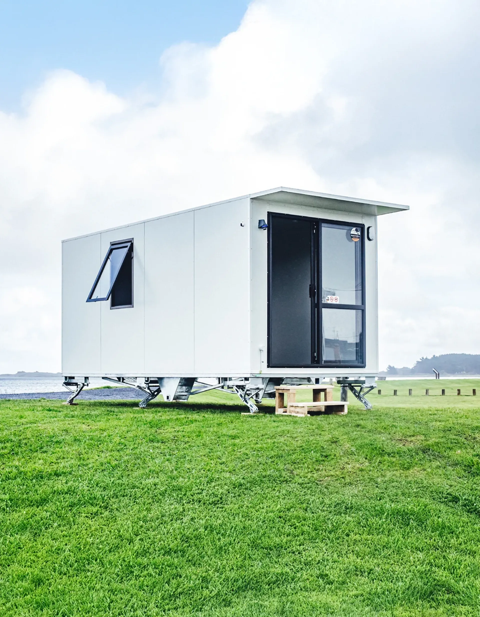 A small white mobile home is parked on a grassy field under a clear blue sky